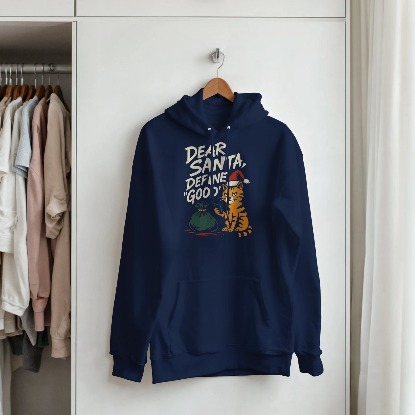 "Dear Santa, Define Good" hoodie hanging on hanger. Minimal LazyWhiskers holiday display.