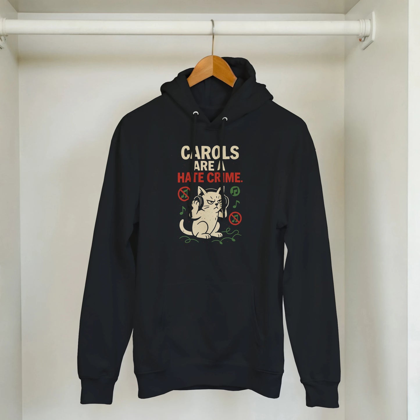 "Carols Are a Hate Crime" hoodie hanging on rack. Minimal LazyWhiskers holiday display.