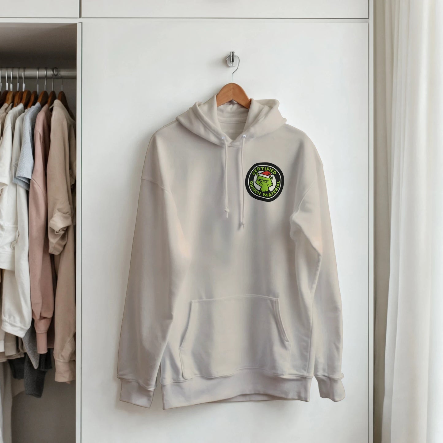 Certified Grinch Mate hoodie hanging on hanger. Minimal LazyWhiskers holiday display.