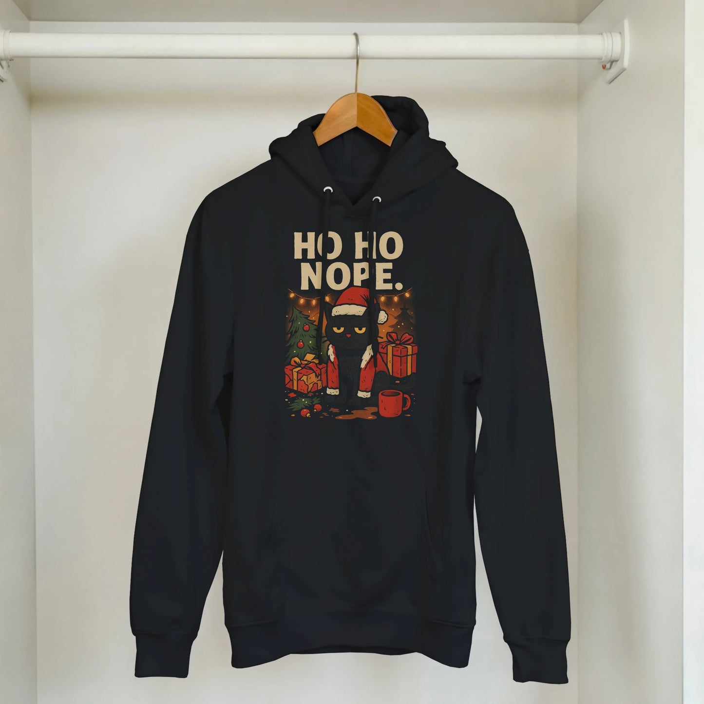 Black ‘Ho Ho Nope’ Christmas hoodie hanging on wooden hanger in minimal home setting