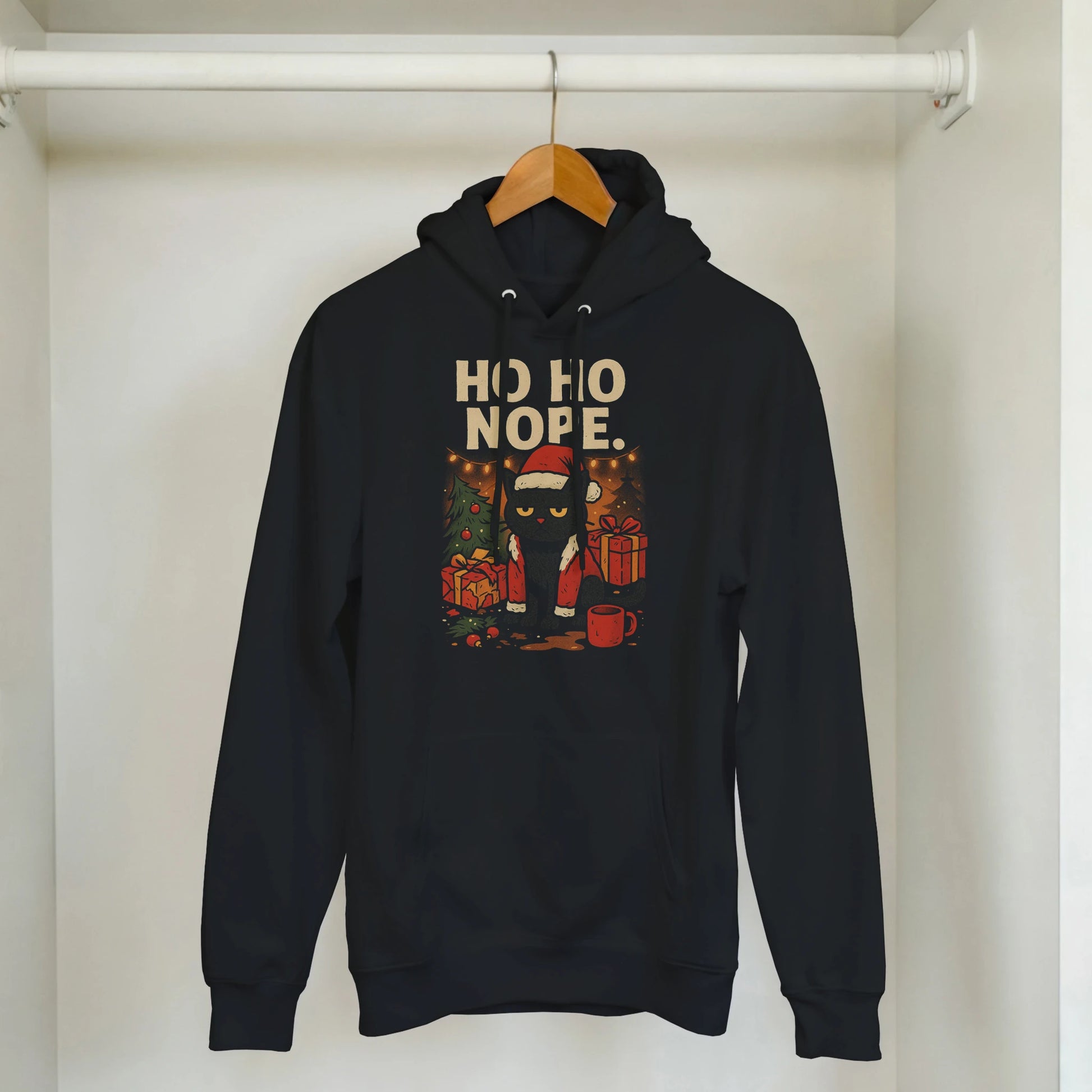 Black ‘Ho Ho Nope’ Christmas hoodie hanging on wooden hanger in minimal home setting