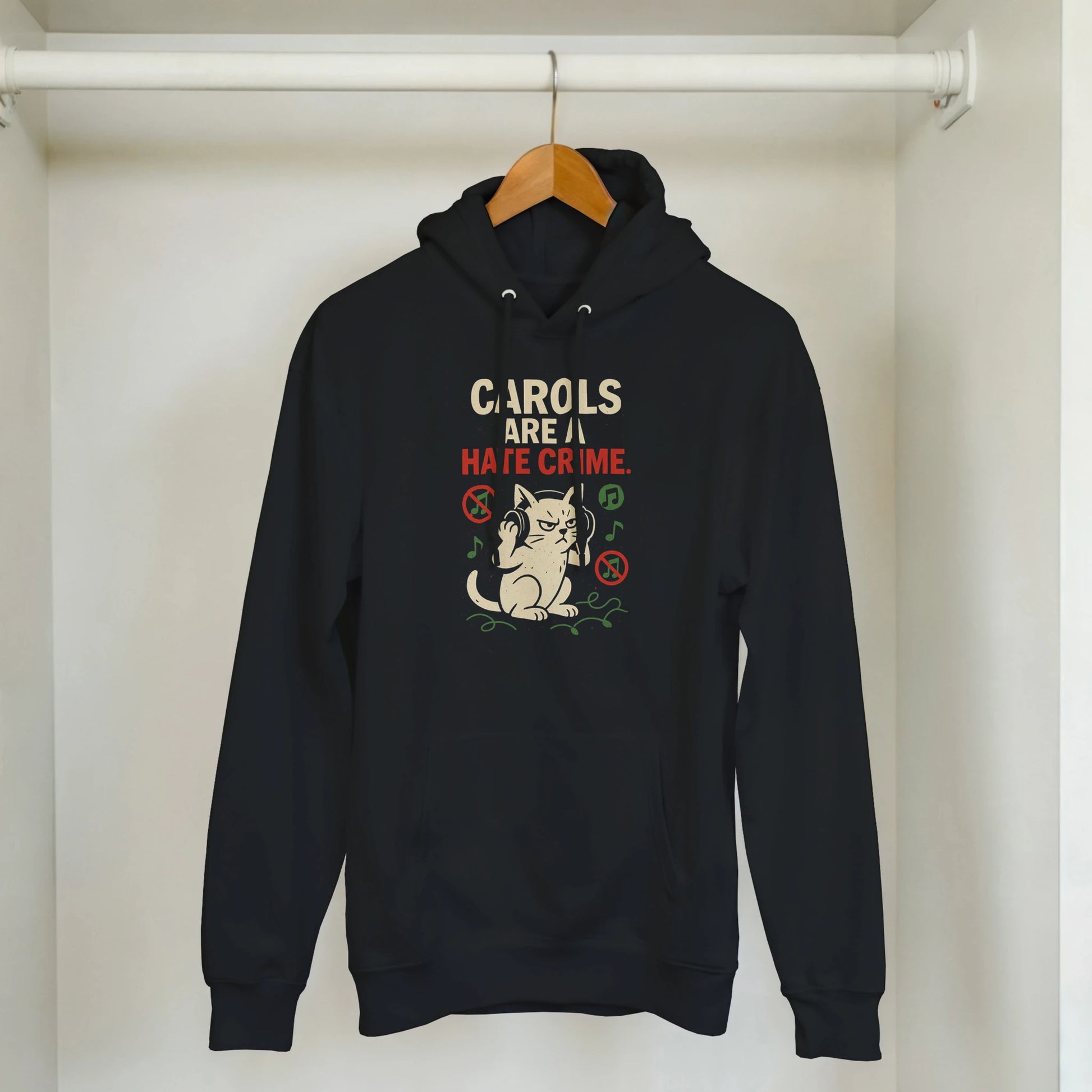 "Carols Are a Hate Crime" hoodie hanging on rack. Minimal LazyWhiskers holiday display.