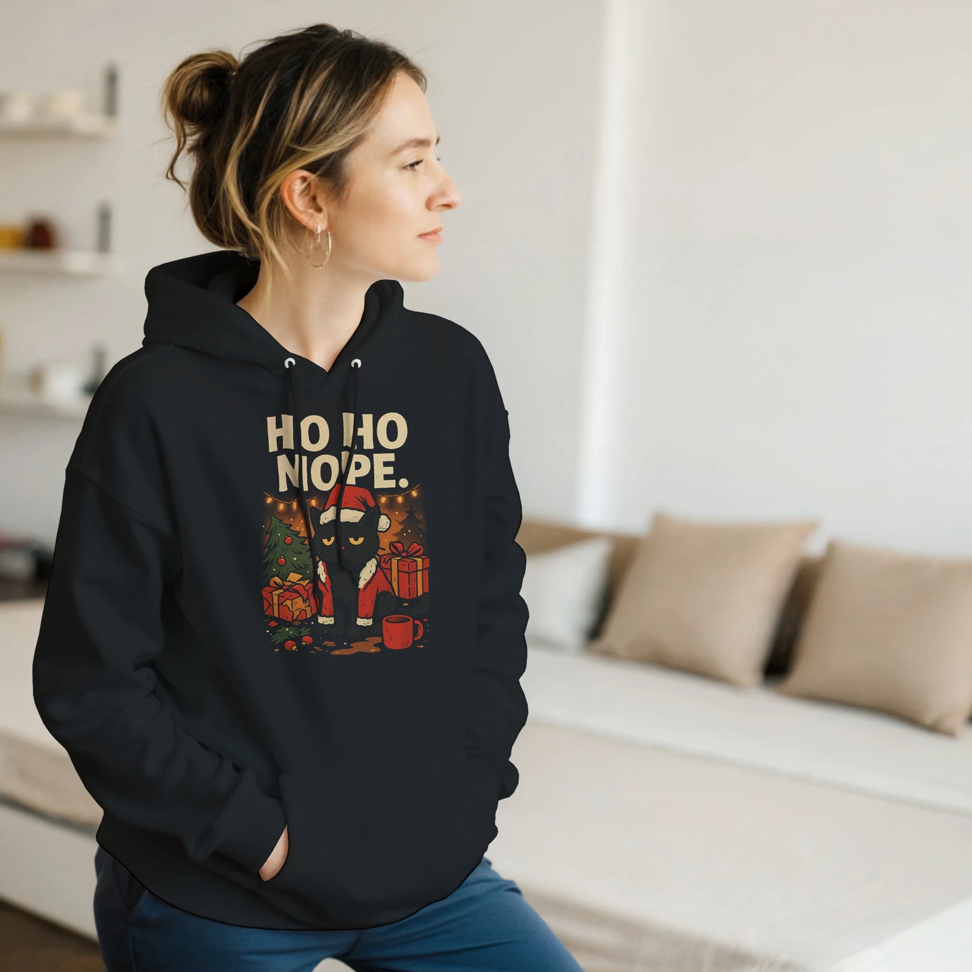 Model wearing black ‘Ho Ho Nope’ Christmas hoodie with grumpy cat holiday design, cozy indoor setting.